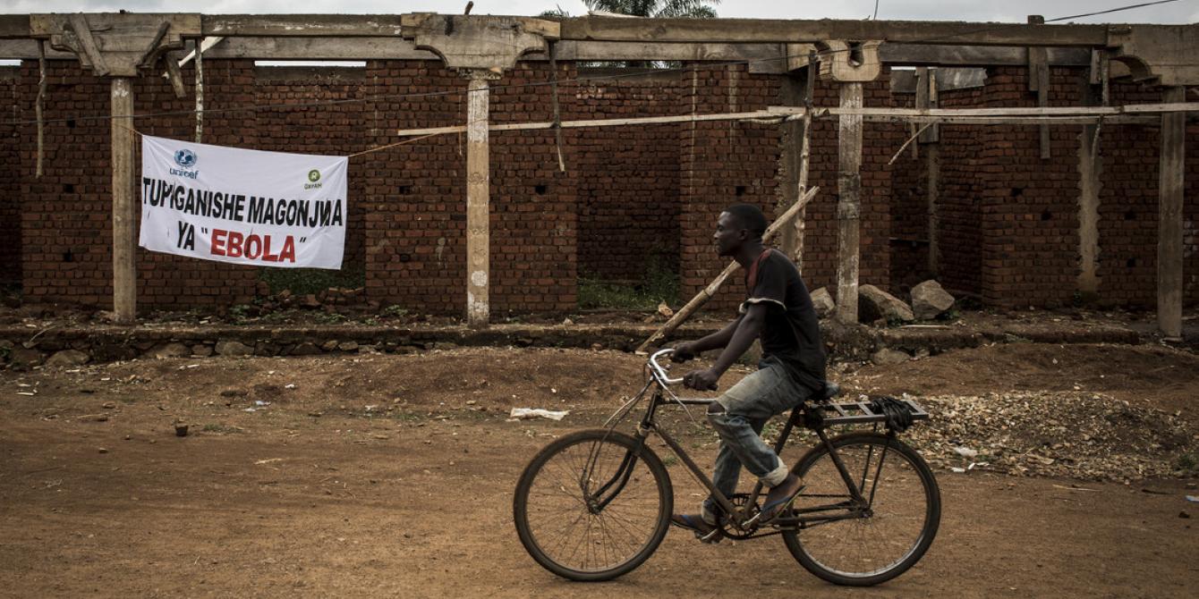 A Congolese man cycles past a sign saying, "the fight against Ebola" in Mangina, DRC. John Wessels/Oxfam